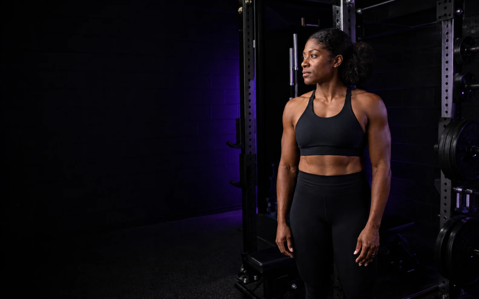 Yvonne standing beside a power rack in a violet-lit strength studio